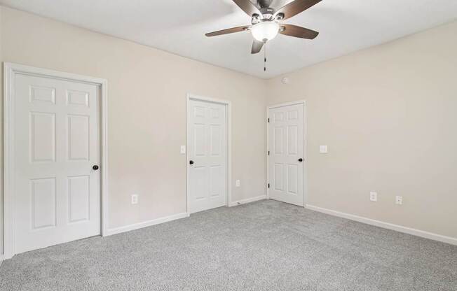 A room with a ceiling fan and three doors.