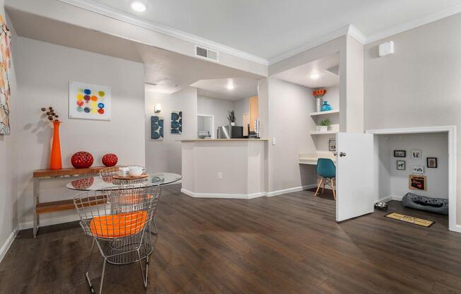 A living room with a white sofa and a glass table with an orange chair.