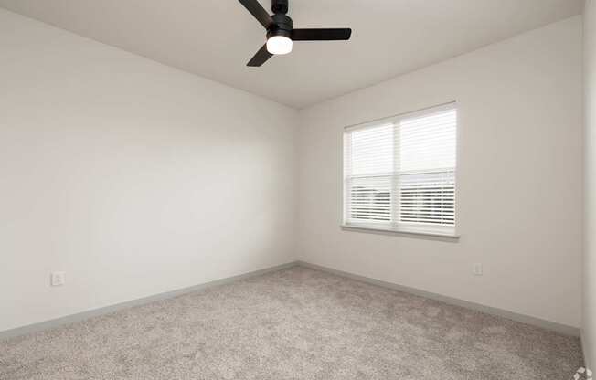 A room with a ceiling fan and a window with blinds.