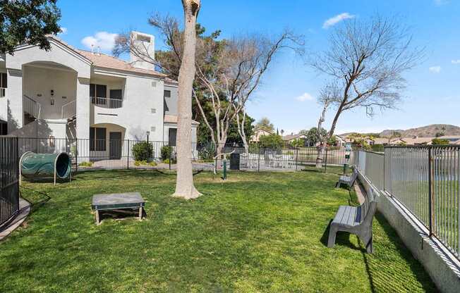 A backyard with a white house, a green lawn, a tree, and a bench.