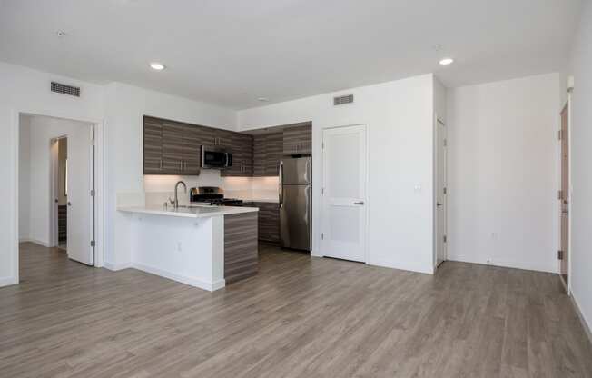 an empty living room with a kitchen and a refrigerator and a sink