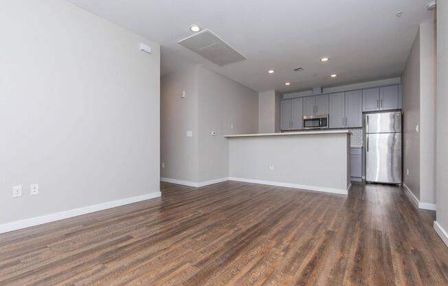 Spacious modern apartment interior featuring hardwood floors, neutral-colored walls, and a kitchen area with stainless steel appliances. The open layout enhances natural light, creating a bright and airy atmosphere.