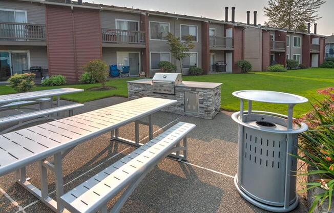 BBQ and picnic area with two picnic tables, a stainless steel BBQ, and a large green lawn and landscaping behind.