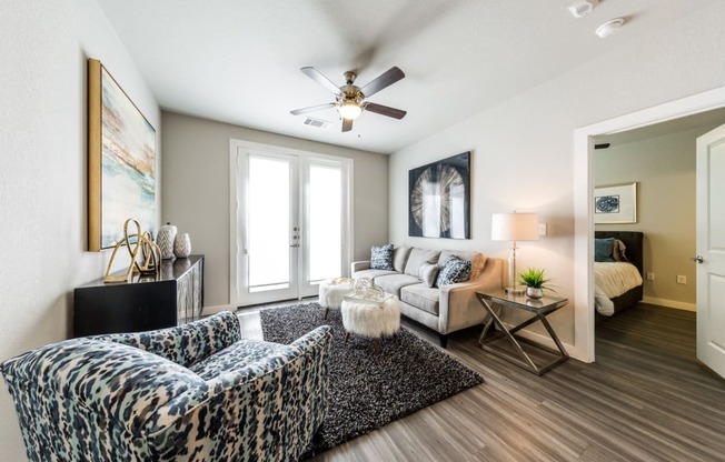 Living room with wood-style flooring, balcony/patio access, ceiling fan, with doorway to bedroom