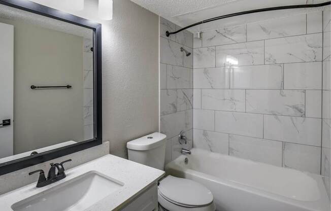 Bathroom with tub-and-shower combo, marble-look tile surround, and single-sink vanity.