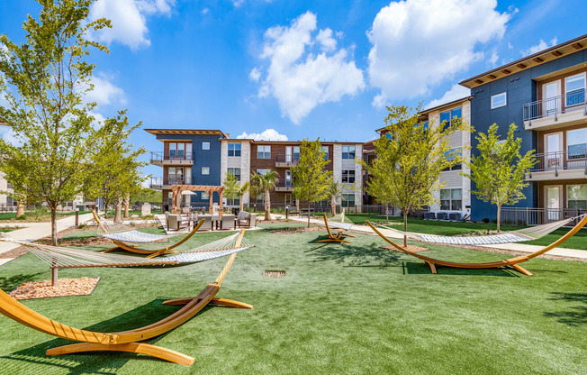 A sunny day at a park with hammocks and apartment buildings in the background.