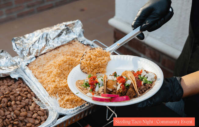 A person is serving food from a plate at a Sizzling Taco Night community event.