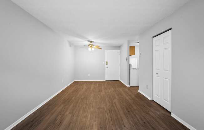 a spacious living room with white walls and wood flooring and a ceiling fan