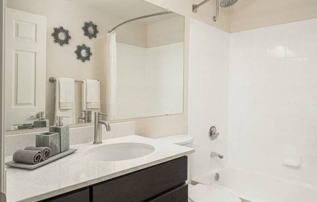 Bathroom with light faux wood floors, brown cabinets, white quartz cabinets and tub/shower