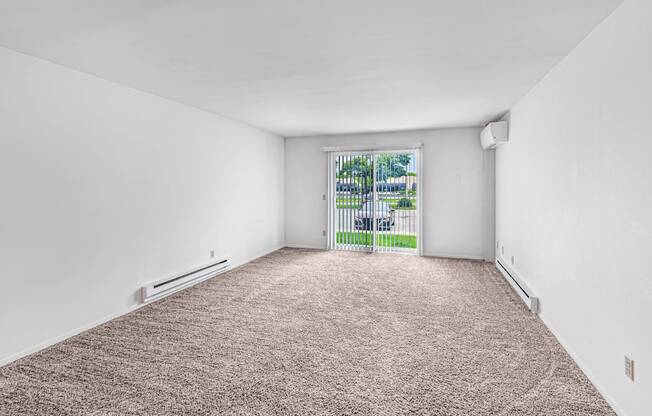 A room with a carpeted floor and a window with a view of a fence and trees.