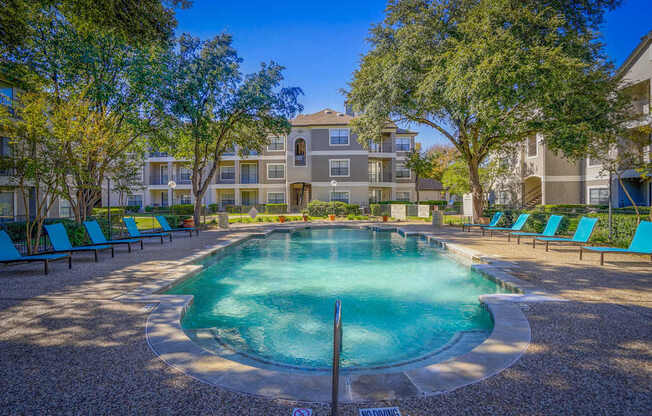 A swimming pool near the clubhouse at Saxony at Chase Oaks Apartments in Dallas, TX, with lounge chairs, lush trees, and landscaped surroundings.