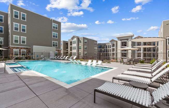 A large swimming pool surrounded by sun loungers and apartment buildings.