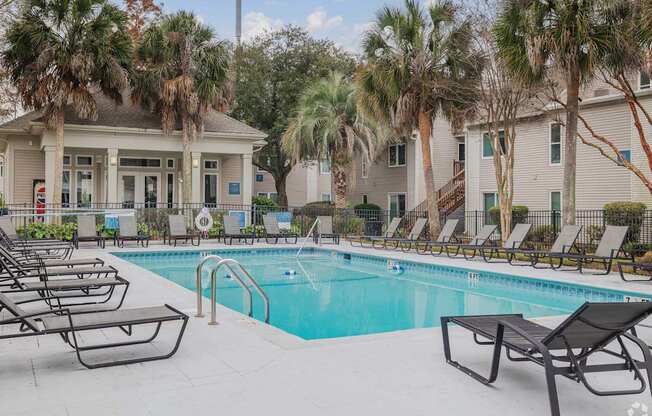 A pool surrounded by lounge chairs and palm trees.