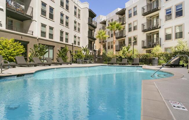 Pet Friendly Apartments in Redwood City CA - mResidences Redwood City - Blue Pool with Gate, Poolside Seating, Tan Building Exterior in the Background