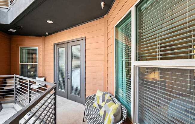 A chair with a yellow and grey blanket is in front of a window with blinds.
