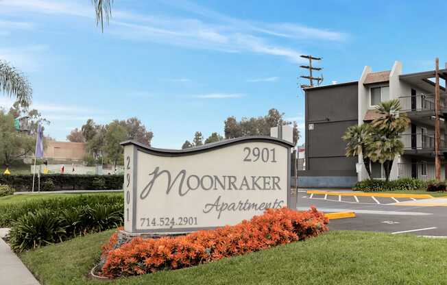 A sign for Moonraker Apartments is surrounded by flowers and greenery.