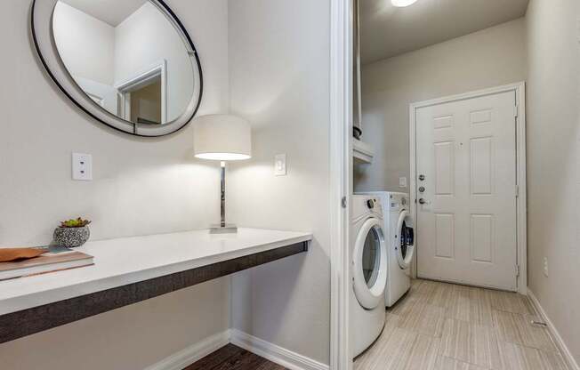 A laundry room with a washer and dryer, a counter, and a round mirror.
