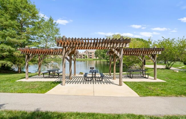 A wooden pergola with benches is situated in a park with a lake in the background at Stonepost Lakeside Apartment Homes, Kansas, 66062.