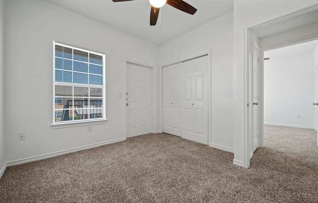 A room with a ceiling fan, carpeted floor, and a window with blinds.