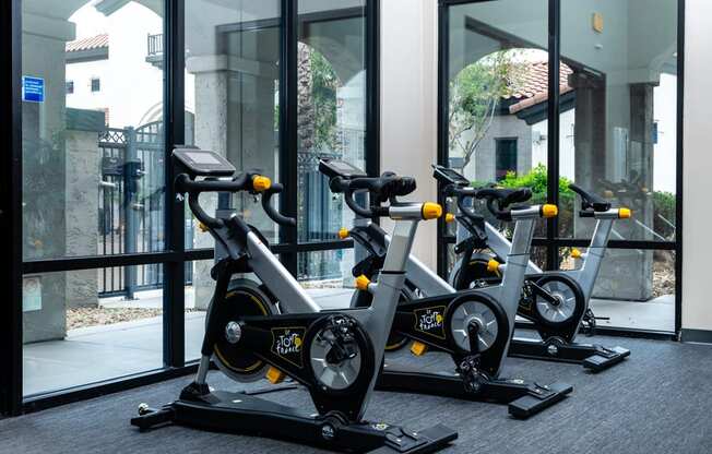 three spin bikes in front of a window in a gym