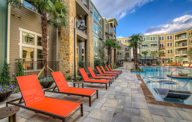 an outdoor swimming pool with chaise lounge chairs and palm trees in front of an apartment building