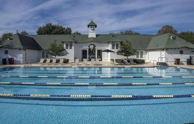 A large swimming pool in front of a white building with a green roof.