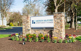A sign for Merion Milford Apartment Homes is surrounded by flowers.