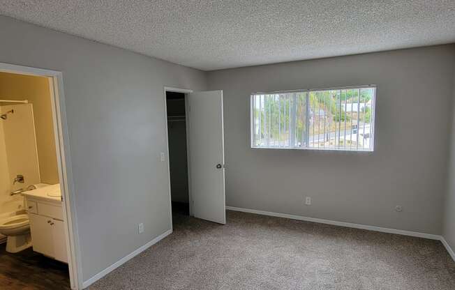 Bedroom with large window and two walk-in closets and entry to shared bathroom at La Mesa Village Apartments in La Mesa, California.