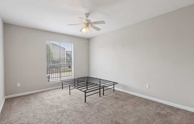 A room with a fan, carpet, and a metal bed frame.