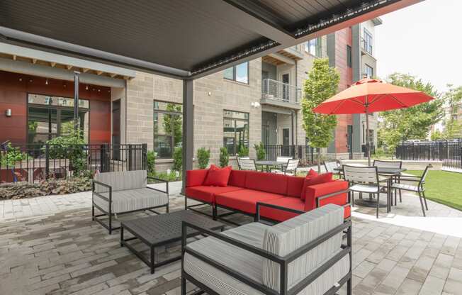 a patio with a red couch and tables with umbrellas