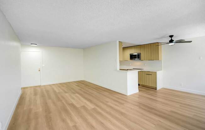 an empty living room with wood flooring and a kitchen