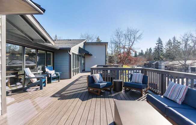 A wooden deck with a white house and blue cushions in the background.