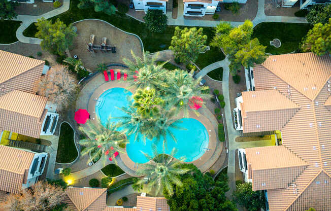 A large swimming pool surrounded by palm trees and a fountain in the middle of a housing complex.