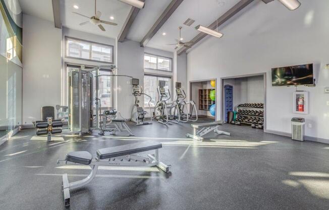 Large fitness center with concrete flooring and ceiling fans. Weight benches, yoga balls, and cardio machines