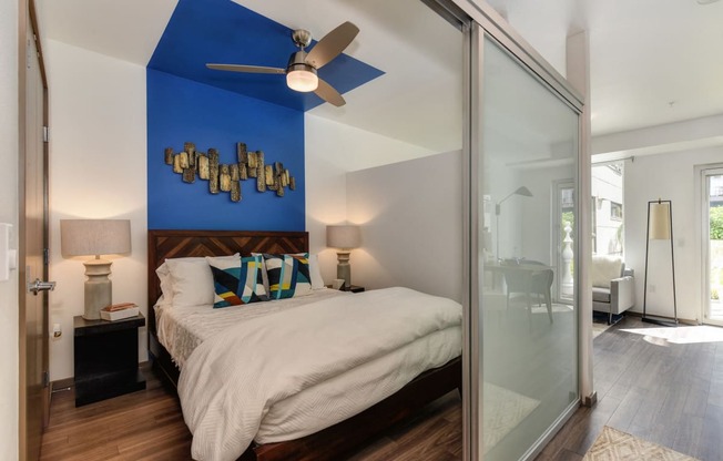 Bedroom  with Sliding Door, Hardwood Inspired Floor, White Comforter Bedding, Blue Wall and Ceiling Fan/Light