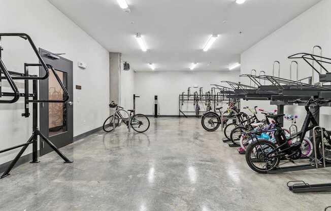 A room with a concrete floor and white walls is filled with bicycles.