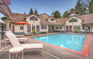 A pool and lounge chairs are in front of a house.