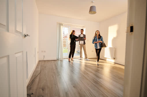 Three people are standing in a room with wooden floors and white walls.