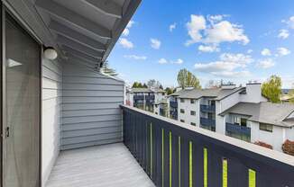 A balcony with a grey wall and a black railing with yellow stripes.