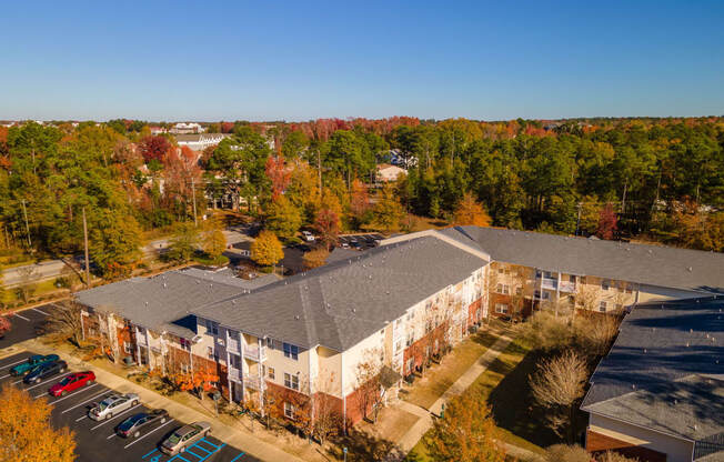 an aerial view of a building with a parking lot and trees in the background