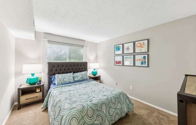 A bedroom with a bed, nightstands, and pictures on the wall.