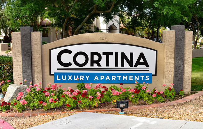 Signage reading Cortina Luxury Apartments with orange and red flowers planted in garden in front of sign