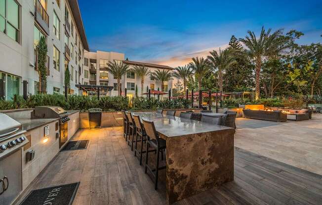 Outdoor grilling station with bar seating, modern appliances, and open-air dining under the evening sky