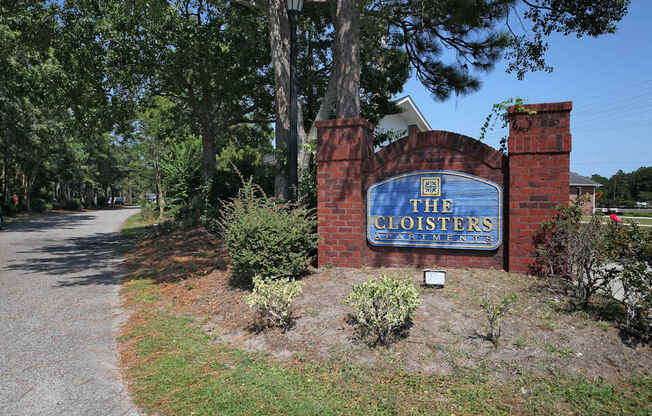 The entrance to The Cloisters with a blue sign on a brick wall. The Cloisters Apartments, 902 67th Avenue North, Myrtle Beach, SC