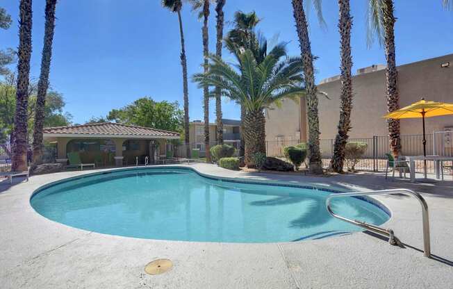 A pool surrounded by palm trees and a building in the background.