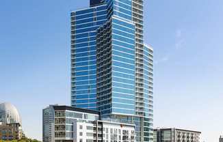 A tall blue building stands in front of a white dome and other buildings.