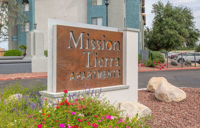 A sign for Mission Tierra Apartments is surrounded by flowers and rocks.