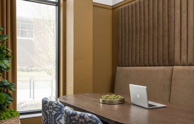 A room with a brown couch, a table with a laptop and a plant on it, and two patterned chairs.