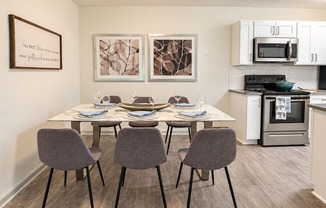Dining table with six chairs beside a kitchen with white cabinets at Icon Avondale Apartments in Decatur, GA.