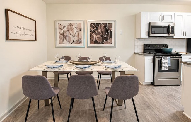 Dining table with six chairs beside a kitchen with white cabinets at Icon Avondale Apartments in Decatur, GA.